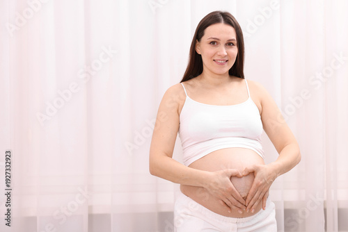 Beautiful pregnant woman making heart gesture near her belly at home, space for text Free Download Beautiful pregnant woman making heart gesture near her belly at home, space for text - GFXLoad