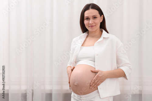 Beautiful pregnant woman touching her belly near curtains at home, space for text Free Download Beautiful pregnant woman touching her belly near curtains at home, space for text - GFXLoad