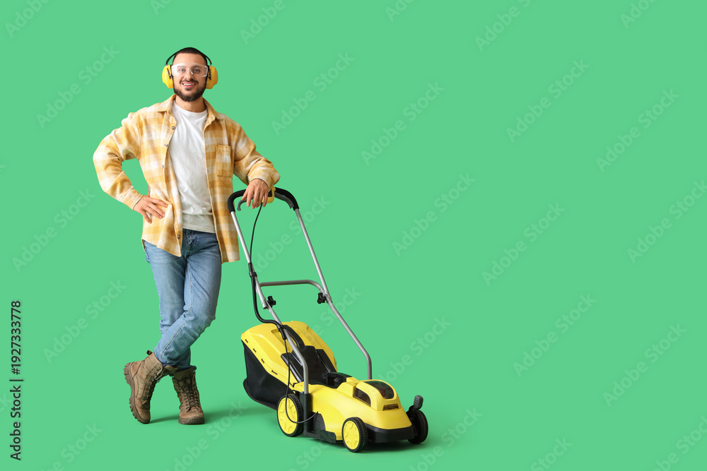 Obraz premium Young man in hearing protectors with lawn mower on green background
