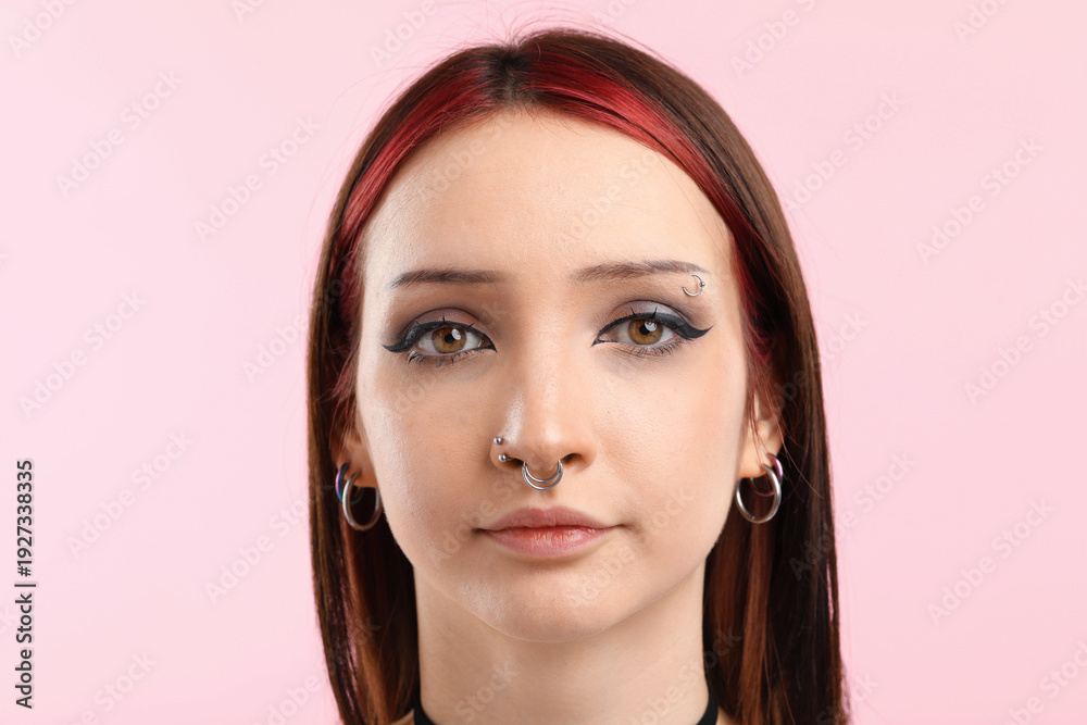 Fototapeta premium Portrait of beautiful young woman with different face piercings on pink background