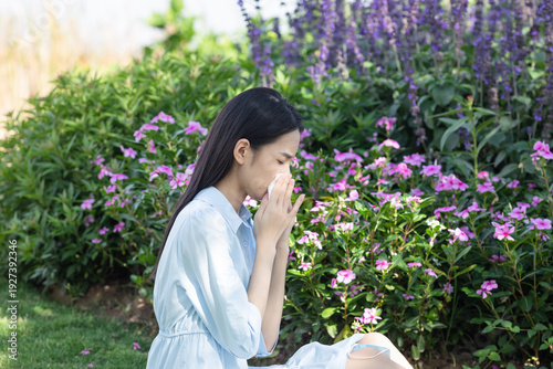 A young woman experiencing nasal allergies beside a flower bush