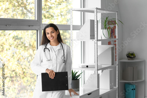 Young female doctor with clipboard near window in clinic