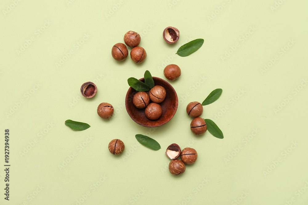 Fototapeta premium Wooden bowl with tasty macadamia nuts and leaves on green background