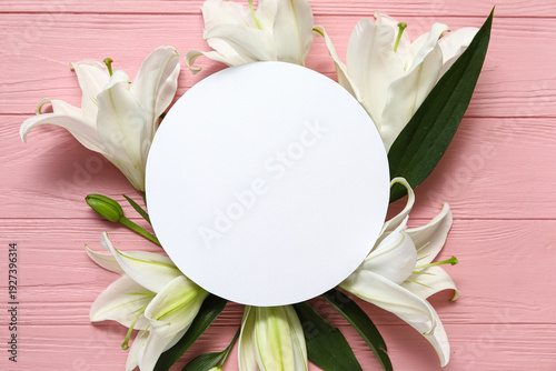 Composition with white lily flowers and blank round card on pink wooden background. Top view