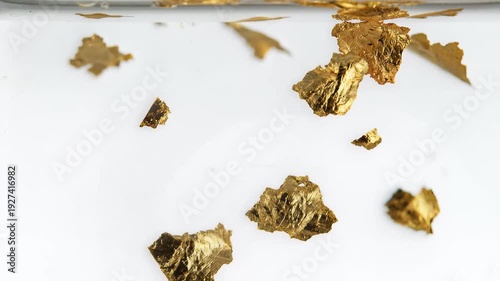 Gold flakes floating in clear liquid against a bright white background for luxury design