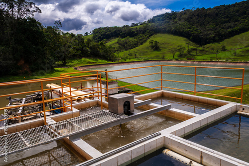 Wallpaper Mural Water purification process at a treatment plant. Industrial facility with settling tanks ensuring clean water supply and environmental protection, with green hills in the background. Torontodigital.ca
