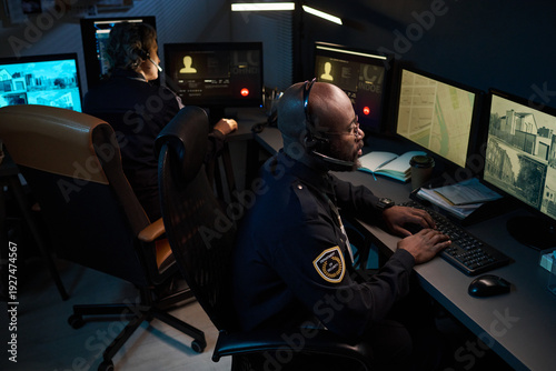 Φωτογραφία Black man wearing headset monitoring security footage on multiple computer scree