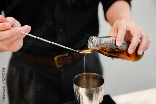 Bartender pouring infused syrup into jigger for cocktail preparation