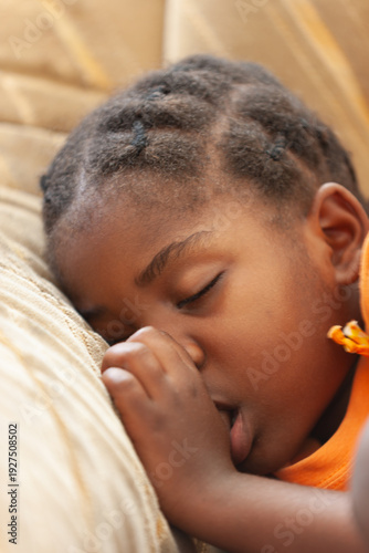 Close-up of a young Black girl with hair twists sleeping on a pillow while sucking her thumb