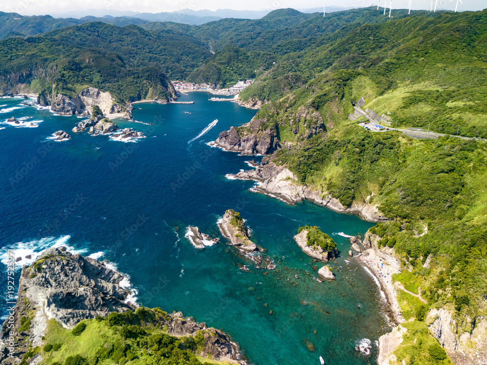 Fototapeta premium 伊豆半島の先端のヒリゾ浜のドローン撮影。 沖には大根島や数々の地磯、陸側には中木港、あいあい岬、ユウスゲ公園が見える。 水面やビーチには遊泳する観光客やライフセーバー。 港と往復する渡船なども見える。 静岡県伊豆半島賀茂郡南伊豆町中木ヒリゾ浜-2025年 