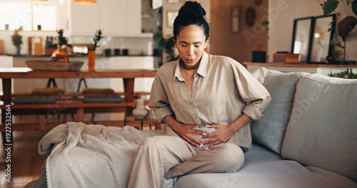фотографія Woman, stomach ache or period with pain on sofa for indigestion or menstruation cycle in home