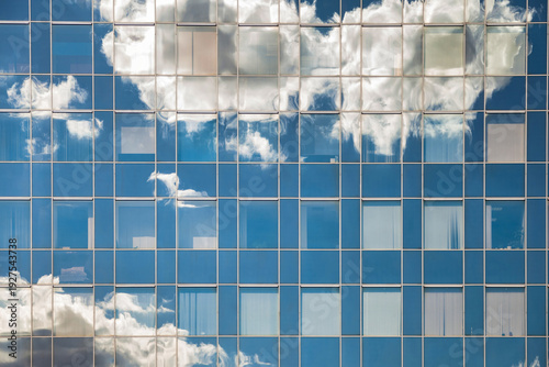 Fotografi Clouds and blue sky are reflected in the numerous windows of a tall office building