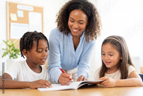 Smiling teacher helping two young students with classwork at school desk