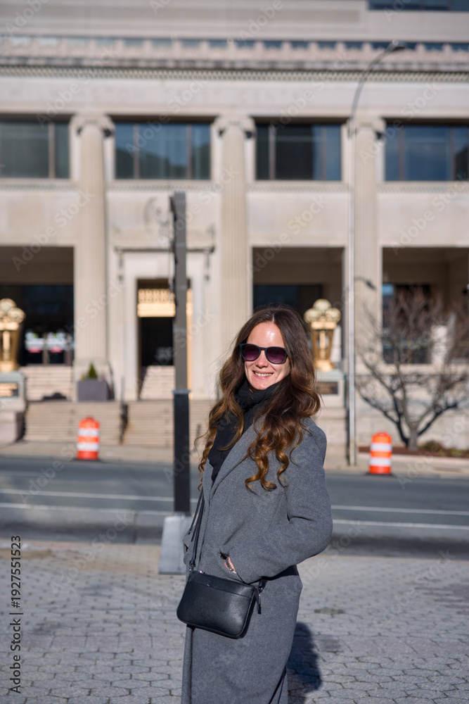 Fototapeta premium Smiling woman in sunglasses wearing gray coat on city street in winter