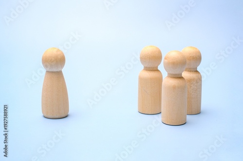 Foto A single wooden peg figure standing apart from a small group of three figures on a light blue background