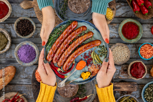 Grilled bratwurst and sausages in the plate at the hands of two women.  
