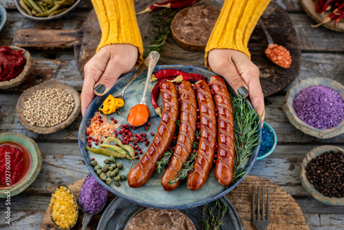 Grilled bratwurst and sausages in the plate at the hands of two women.  
