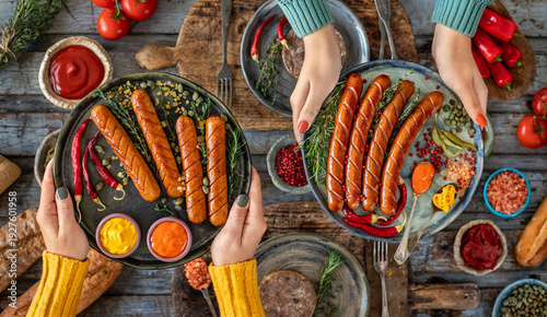Grilled bratwurst and sausages in the plate at the hands of two women.  
