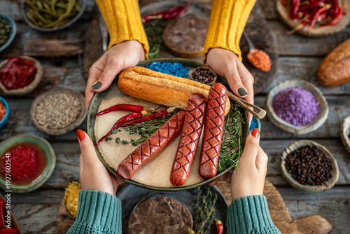 Grilled bratwurst and sausages in the plate at the hands of two women.  
