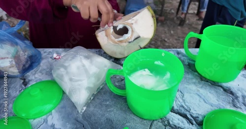 Coconut being cracked open on a table with green cups.