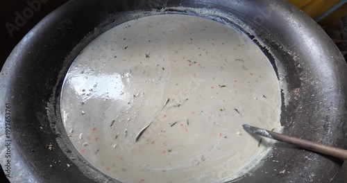 Mixing a batter or dough in a metal bowl with a spoon.