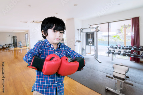 Young Boy in Plaid Shirt Wearing Red Boxing Gloves in a Gym