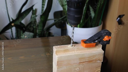 Drilling a hole into a wood block secured with clamp. Diy carpentry project, woodworking workshop process with tools.