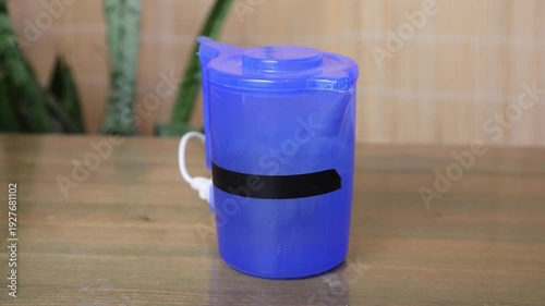 Small plastic electric kettle on a wooden table, initially still, then boiling with bubbling water, and finally returning to a calm state