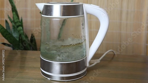 Kettle with water boiling and bubbling inside on a wooden surface, showing the heating process for a hot drink.