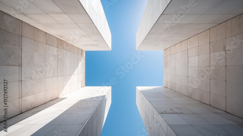 A symmetrical perspective looking straight up between four white marble or stone pillars toward a bright blue sky, highlighting clean lines and architectural height.