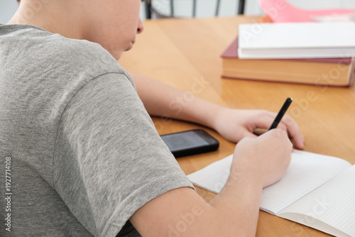Φωτογραφία A teenager does his math homework, writes down examples in a notebook, and uses his smartphone for educational purposes