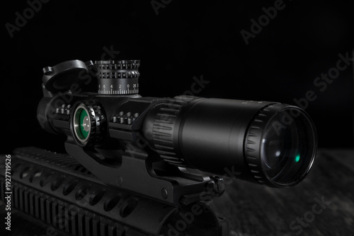 Close up of a tactical rifle scope mounted on a rail system against black background