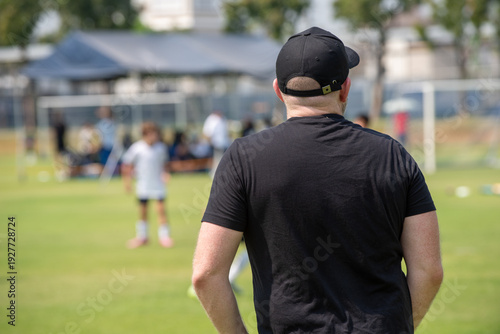 Candid back view of a supportive father cheering for their son during a youth soccer match at school.