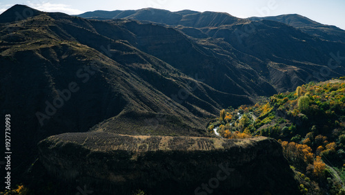 Mountain valley landscape with autumn forest and dramatic hills under blue sky