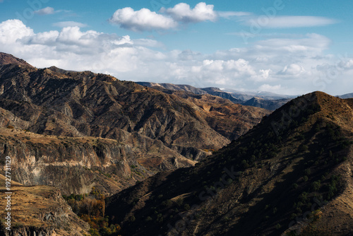 Mountain valley landscape with autumn forest and dramatic hills under blue sky