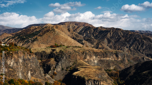 Mountain valley landscape with autumn forest and dramatic hills under blue sky