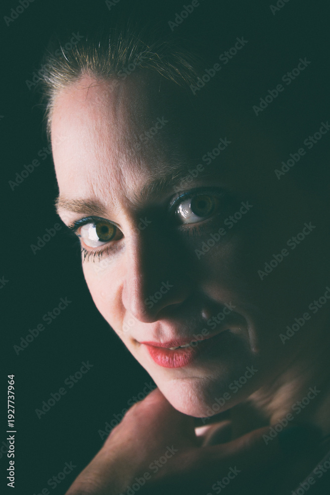 Obraz premium Low-Key-Portrait eines Models im Mantel vor dunklem Hintergrund. Dramatisches Licht, starke Schatten und roter Lippenstift setzen elegante, ausdrucksstarke Akzente.