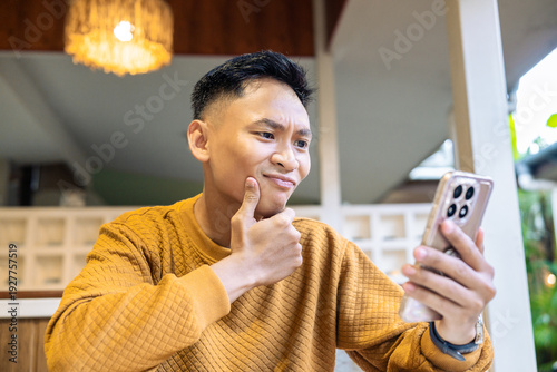 Εκτύπωση καμβά Confused Asian man thinking while looking at his smartphone