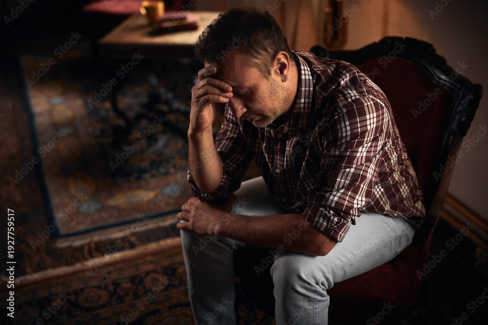 Obraz premium Man with headache, depression, sadness and loneliness sitting on a chair at home.