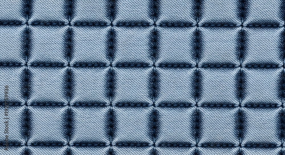 Fototapeta premium Quilted denim texture with a repeating grid pattern, showcasing the weave of the fabric and soft blue tones for a cozy background.