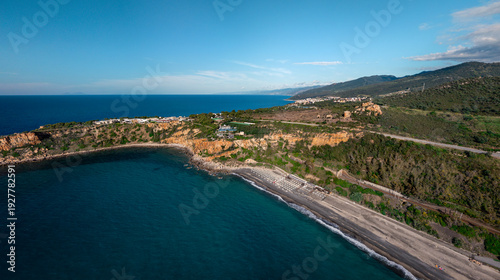 Aerial view of Spiaggia Torre Conca where cerulean waters meet rugged cliffs and a dark sandy beach, Finale, Sicilia, Italy.