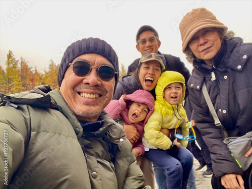Multigenerational Asian family enjoying a winter vacation at Mt. Fuji Subaru Line 5th Station, Yamanashi, Japan. Happy family taking a group selfie with colorful autumn trees in November.