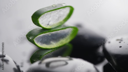 Aloe Vera slices and spa stones closeup. Aloevera plant leaf gel, natural organic renewal cosmetics, alternative medicine. Skin care concept. Rotating on black background. Moisturizing
