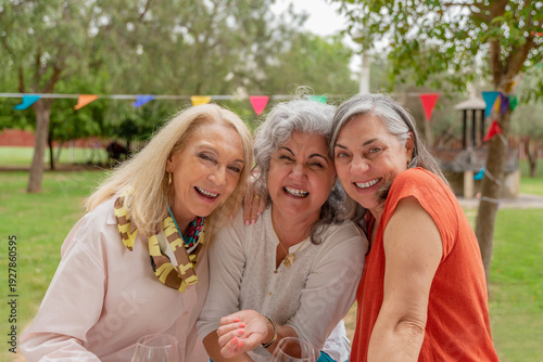 Happy mature female friends embracing and smiling at festive garden gathering