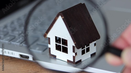 Man hand holding magnifying glass with house model. House online search. Property value, home buying and selling, real estate investment concepts.
