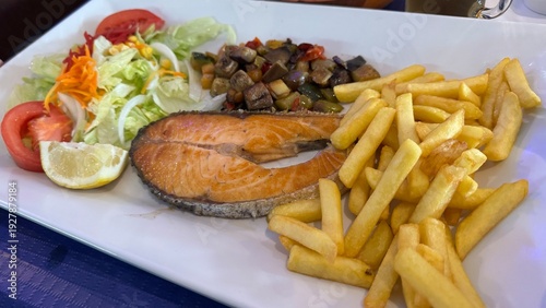 Gourmet Salmon Delight: A beautifully presented plate features a perfectly grilled salmon steak alongside crispy fries, fresh salad, and sautéed vegetables, showcasing culinary excellence.