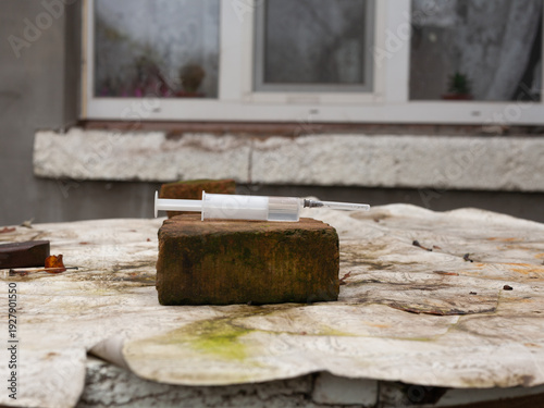 Foto An unused plastic syringe lies on a brick in the street.