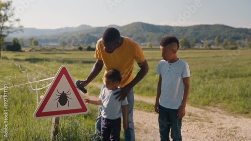 African American father warning his two sons about Lyme disease, showing them a tick warning sign, handheld shot.