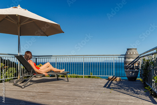 Woman sunbathing on veranda with ocean view