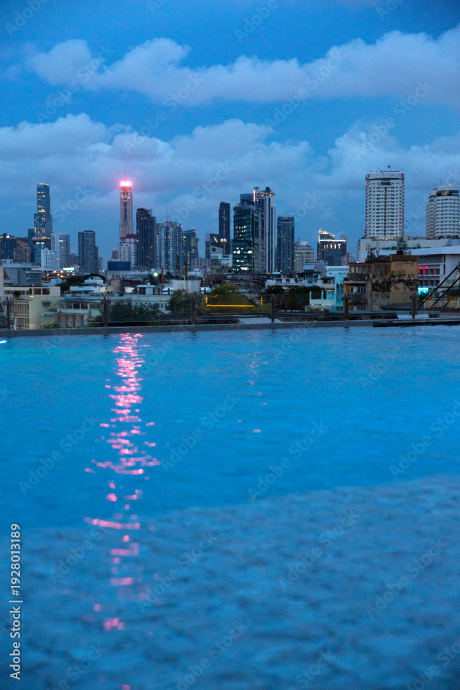 Fototapeta premium Skyline of Bangkok at dusk. The cityscape features numerous skyscrapers of varying heights, including prominent slender towers and denser office buildings, all silhouette against a deep blue sky.